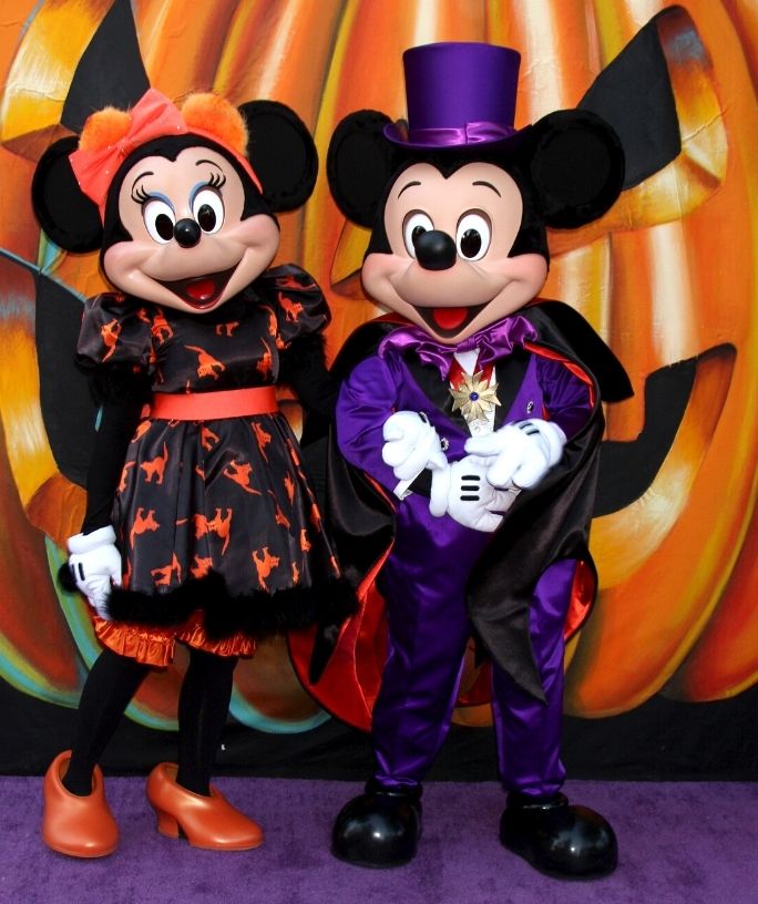 Mickey and Minnie Mouse dressed in Halloween attire, standing in front of a pumpkin backdrop, at Disney World