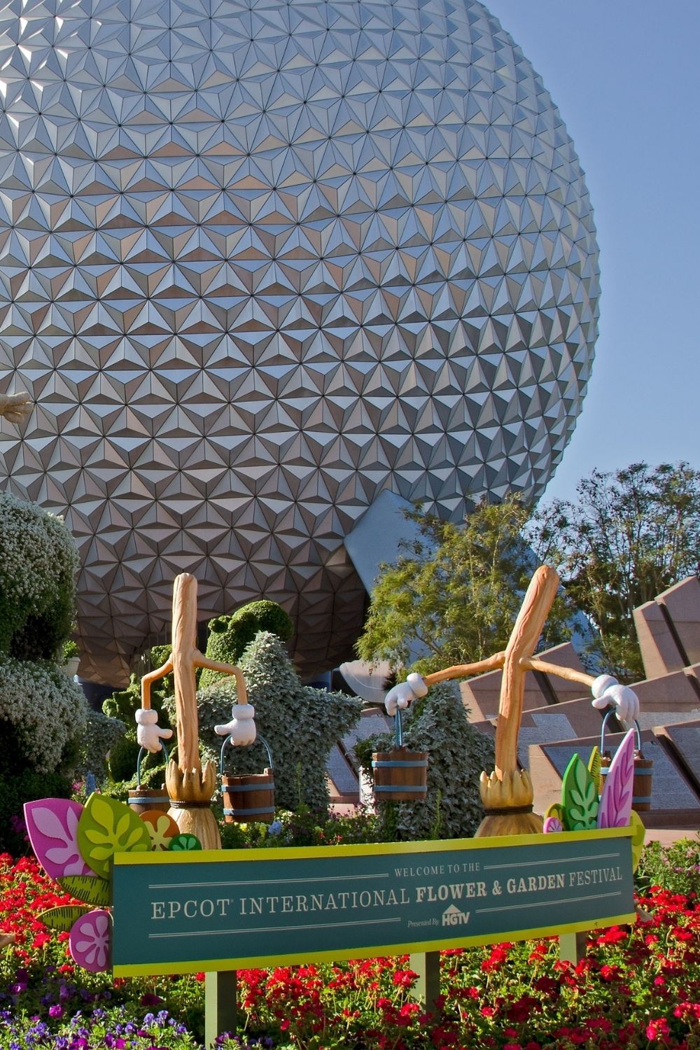 a sign for the Epcot International Flower and Garden Festival is positioned in front of Spaceship Earth