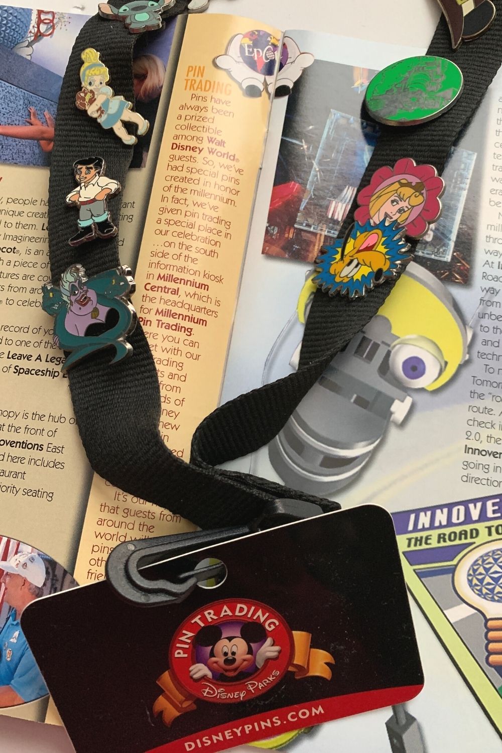 a Disney pin trading lanyard rests on a 2000 Epcot commemorative program, which discusses the beginning of pin trading in Disney World.