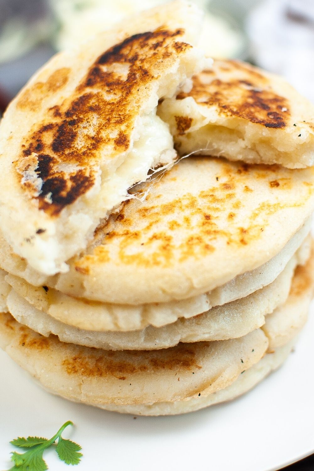 a stack of arepas con queso, with the top arepa broken open to show the fluffy, cheesy interior