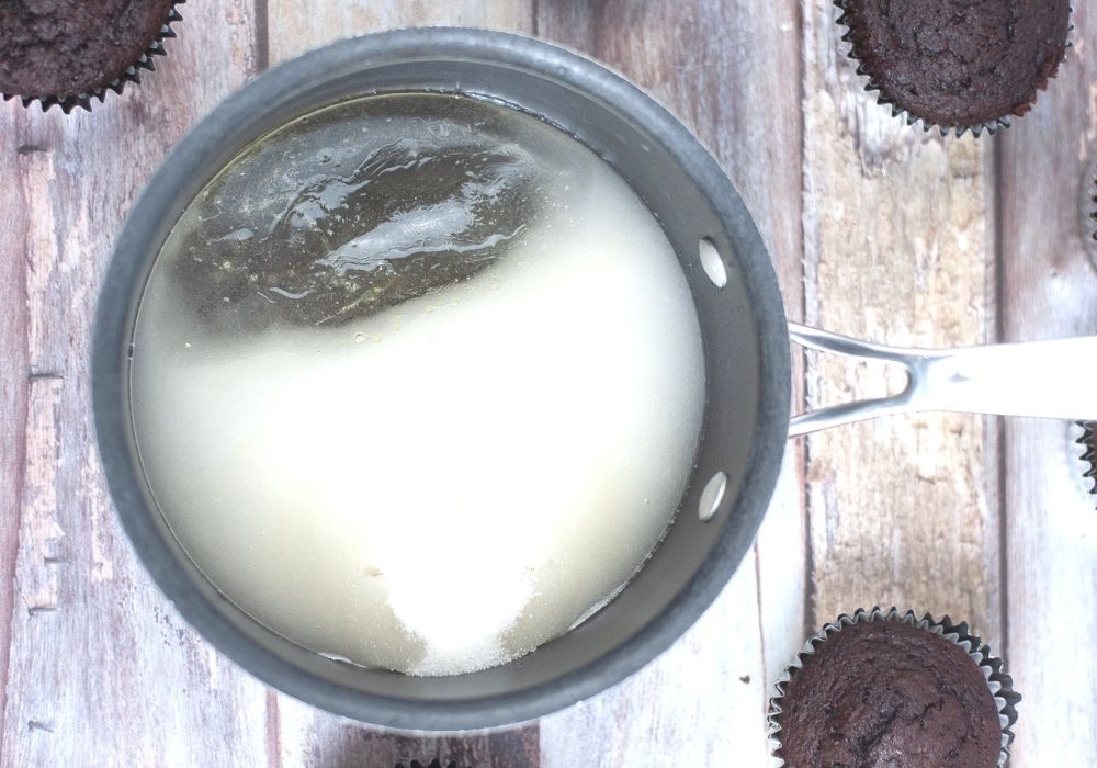 sugar, corn syrup, water, and cream of tartar in a saucepan with chocolate cupcakes around it.