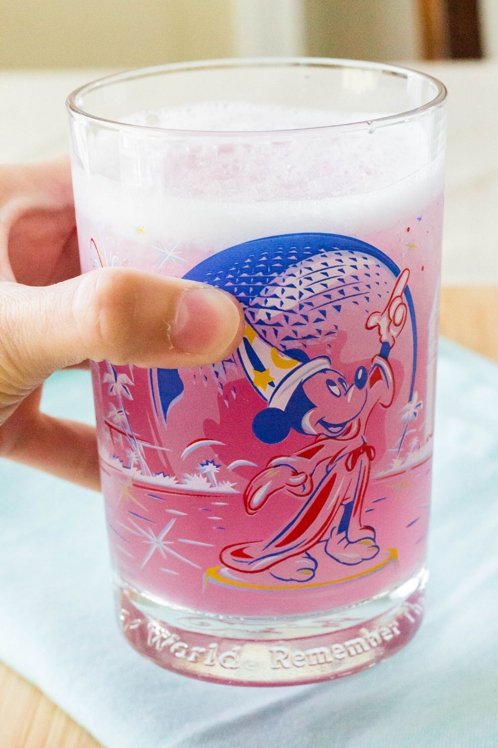 a woman's hand holds a Disney glass filled with violet lemonade like what is served at Epcot