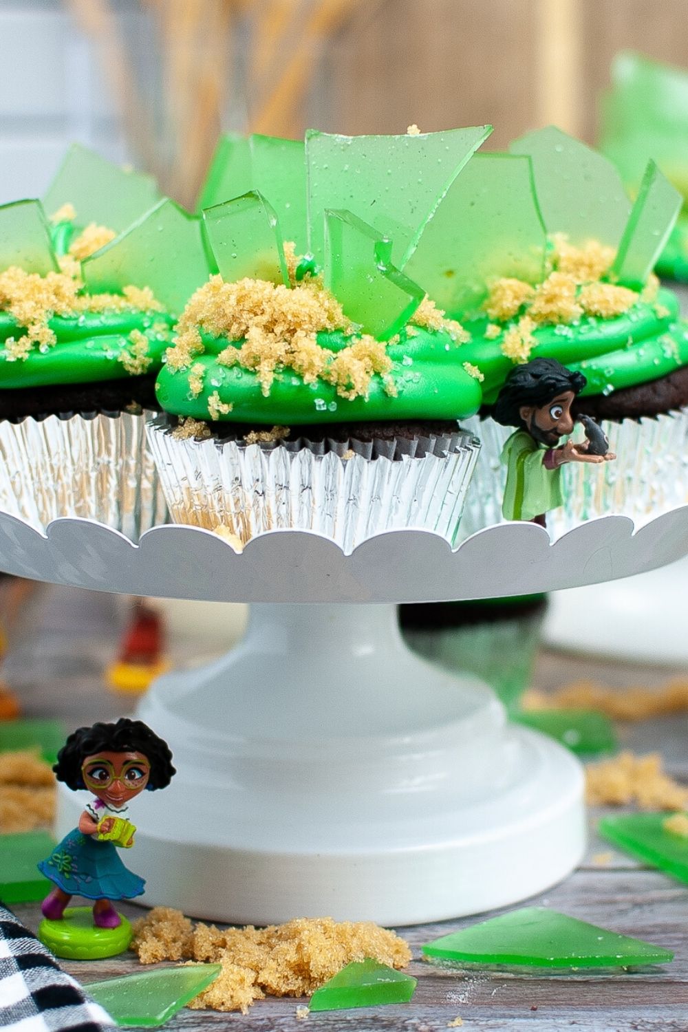 decorated Encanto cupcakes displayed on a white cake stand with Mirabel and Bruno figurines from the Family Madrigal.