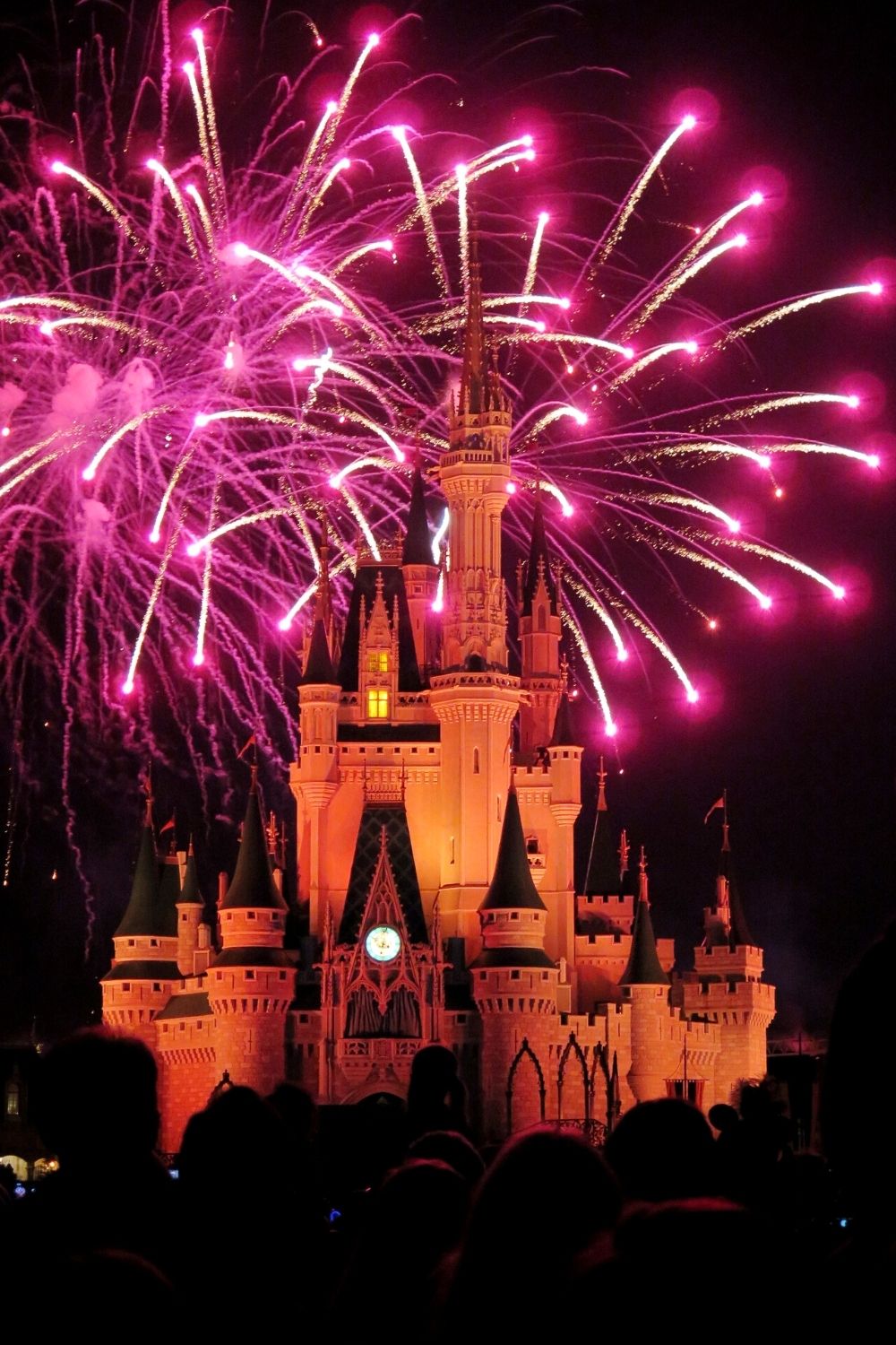 Cinderella's Castle in Magic Kingdom is lit orange with pink fireworks overhead