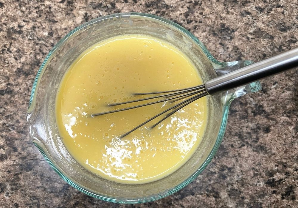 Dole Pineapple soft serve mix dissolved in liquid in a mixing bowl, with a whisk in the bowl