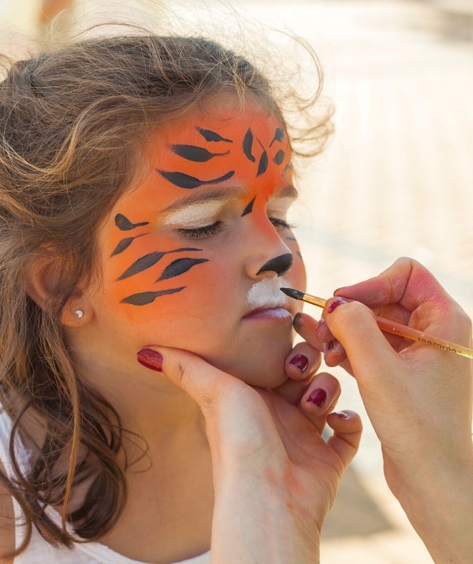 a child gets their face painted in a tiger design