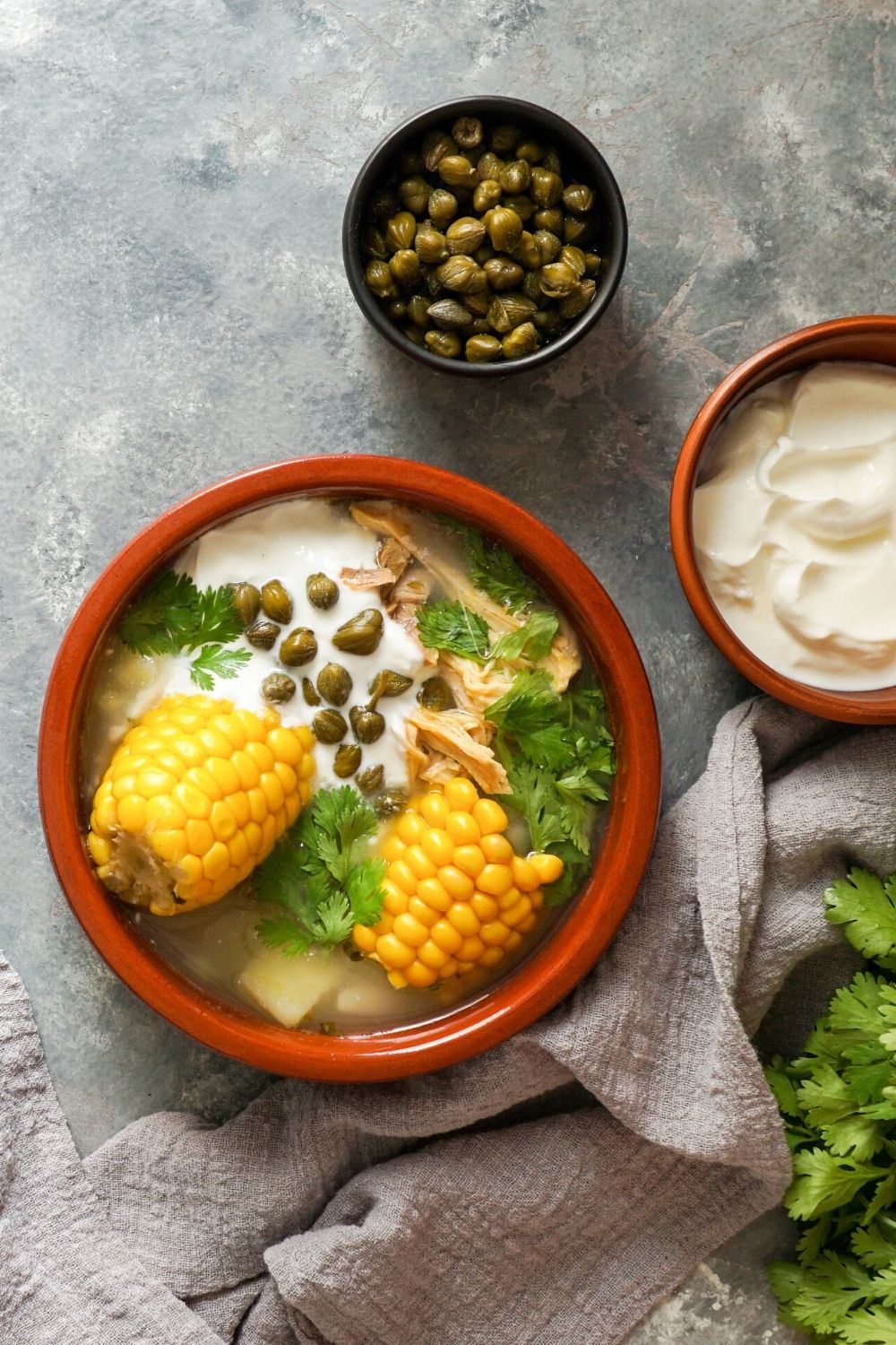 overhead view of a bowl of ajiaco soup with a bit of cream in it, along with some capers as a garnish