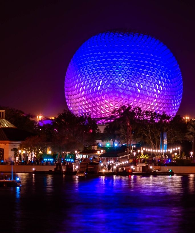 Epcot's Spaceship Earth lit up in pink, purple, and blue at night