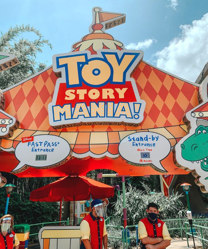 two cast members stand under an attraction sign for Toy Story Mania at Disney World, which displays the estimated wait times