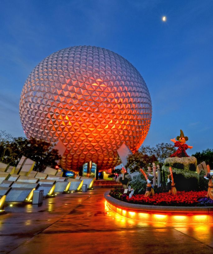 Spaceship Earth at Epcot in Disney World is lit up at night, with a red-orange light shining on it