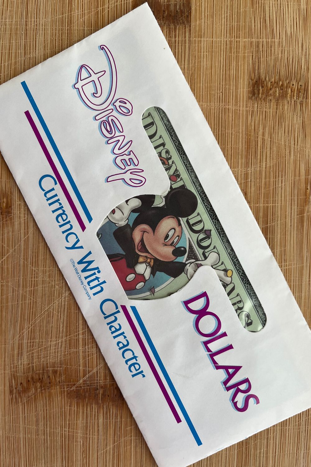 A Disney Dollar inside of an envelope marked "Disney Dollars: Currency with Character"