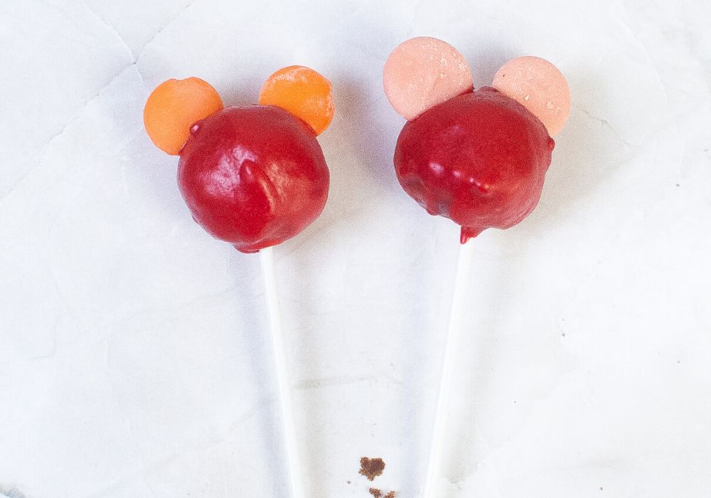 Two early-stage Mickey Mouse cake pops, which have been dipped in red almond bark and have candy melts stuck in the sides to form ears