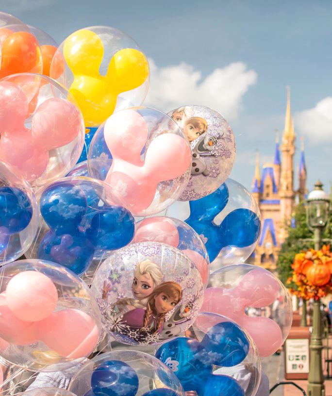 close-up view of Disney World balloons for sale on Main Street USA, including pink, yellow, blue, and orange Mickey Mouse balloons, plus Frozen-themed character balloons.