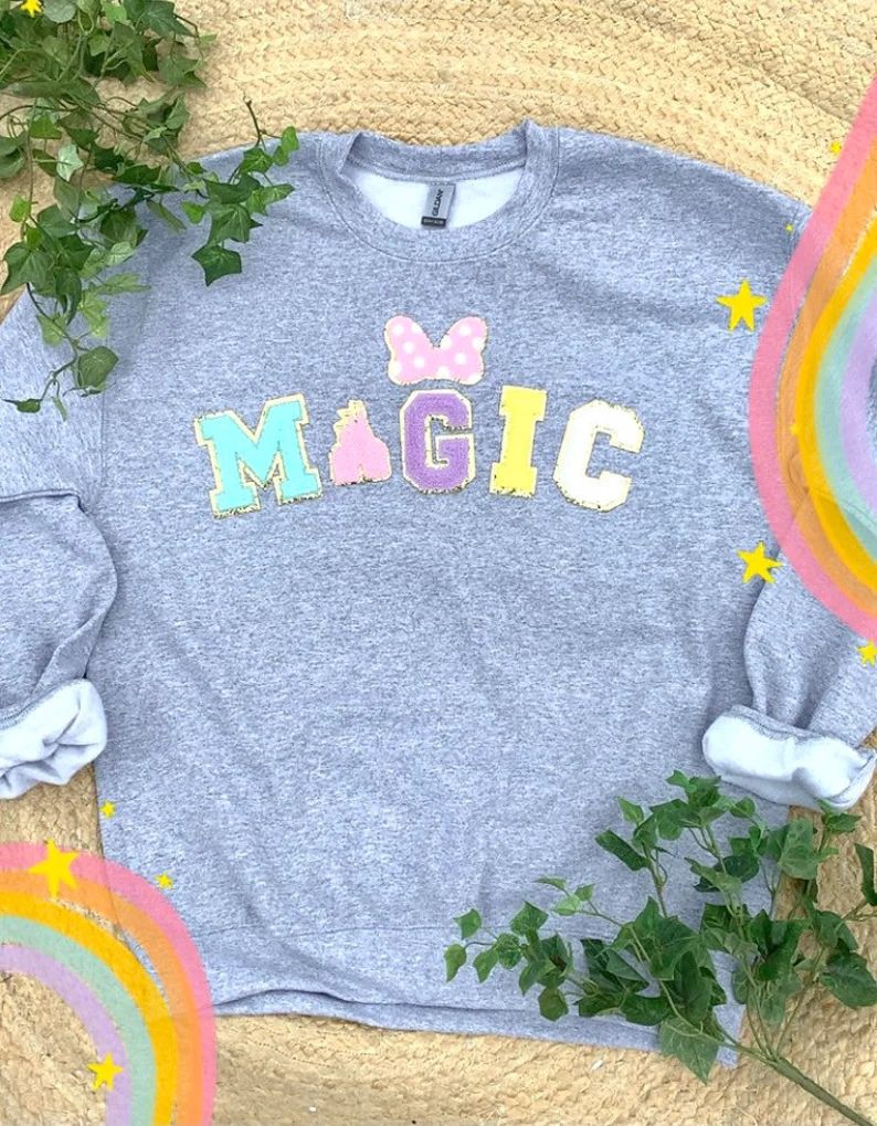 picture of a grey sweatshirt with multicolor disney patches spelling magic