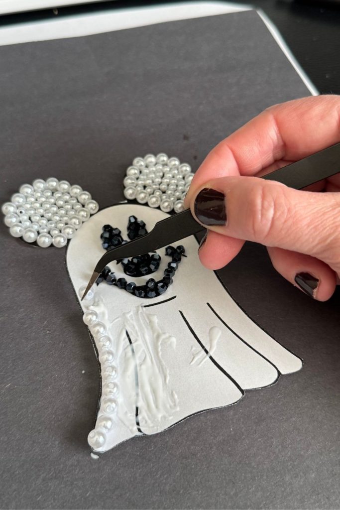 picture of someone putting pearl beads onto their mickey ghost diy